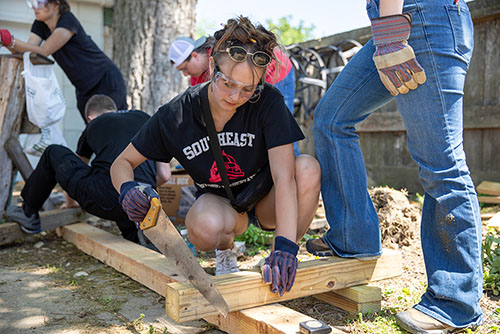 Participant of the historical preservation field trip cuts a piece of wood.