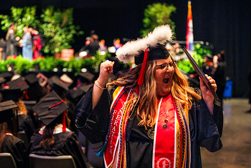 Woman cheering as she holds her diploma.