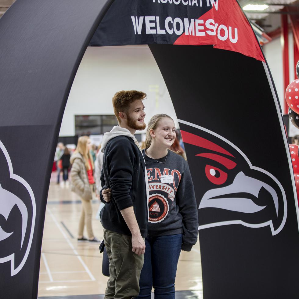Two students pose for a photo under an arched SEMO banner at Show Me Day in the Recreation Center. 