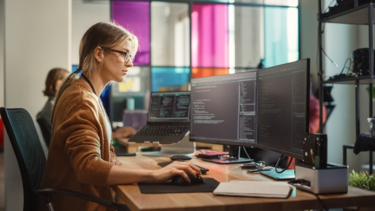 A computer programmer works at a computer in an office.