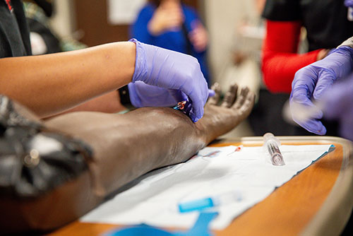 two semo nursing students work together on a mannequin in a simulation of a hospital room in SEMO's nursing lab