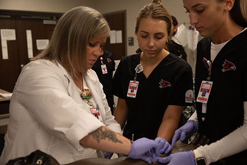 two nursing students practice techniques on a mannequin