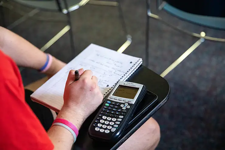 A students arms rest on a desk with a calculator and a notebook in a mathematics class at SEMO.